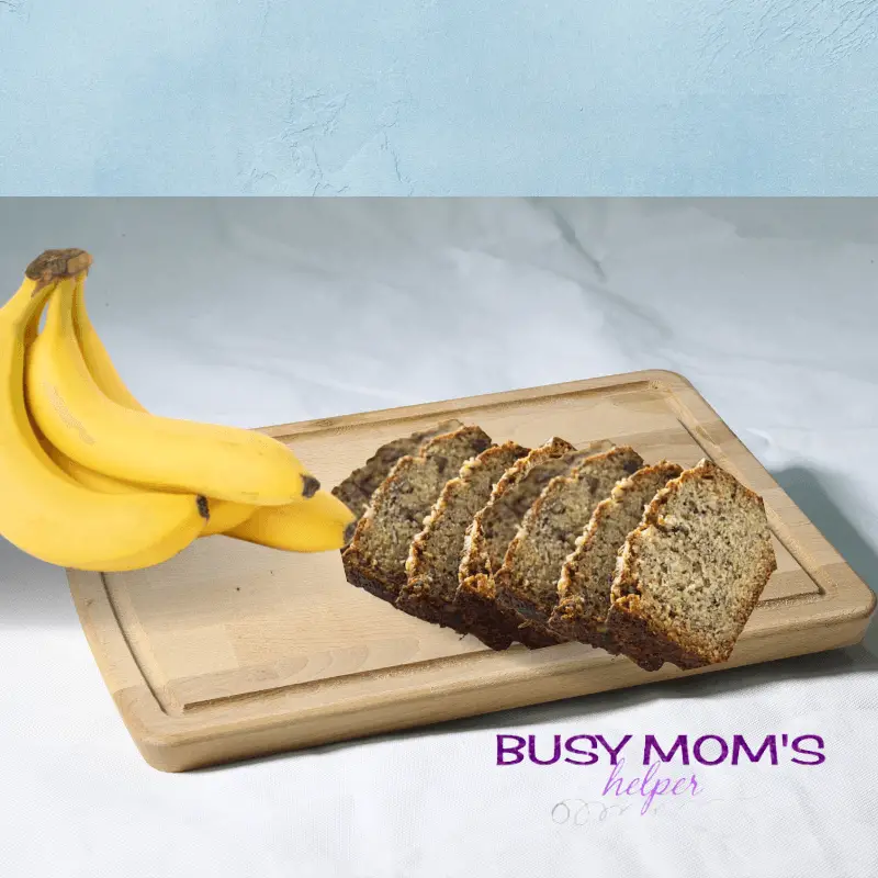 photo of sliced banana bread on a wood cutting board with a bunch of bananas