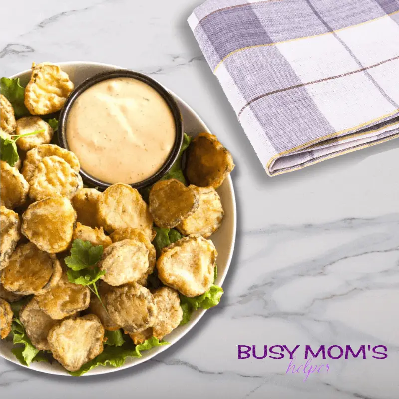 photo of fried pickles in a white bowl with orange dipping sauce on a marble counter top