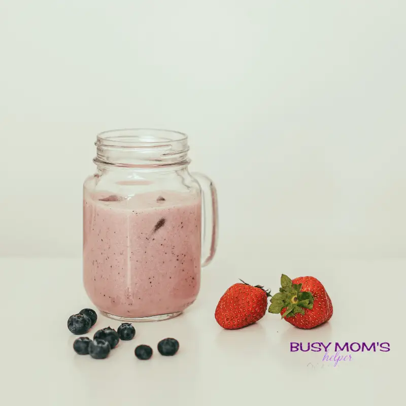 photo of a pink smoothie in a glass, next to berries.