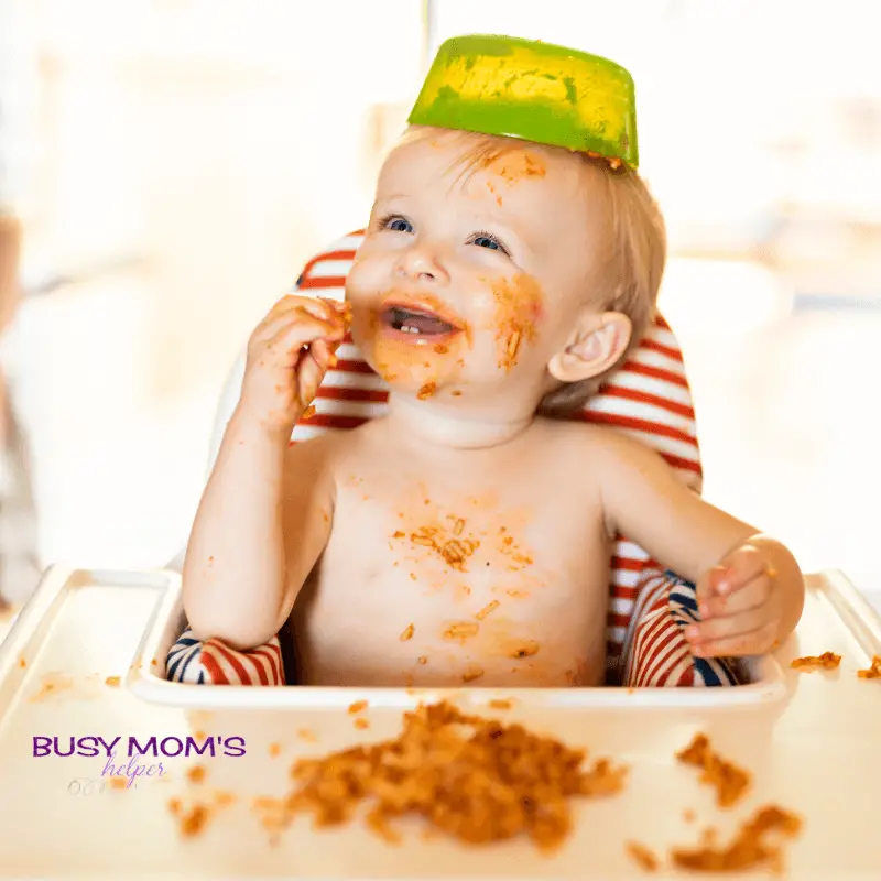 photo of a baby eating spaghetti in a high chair.